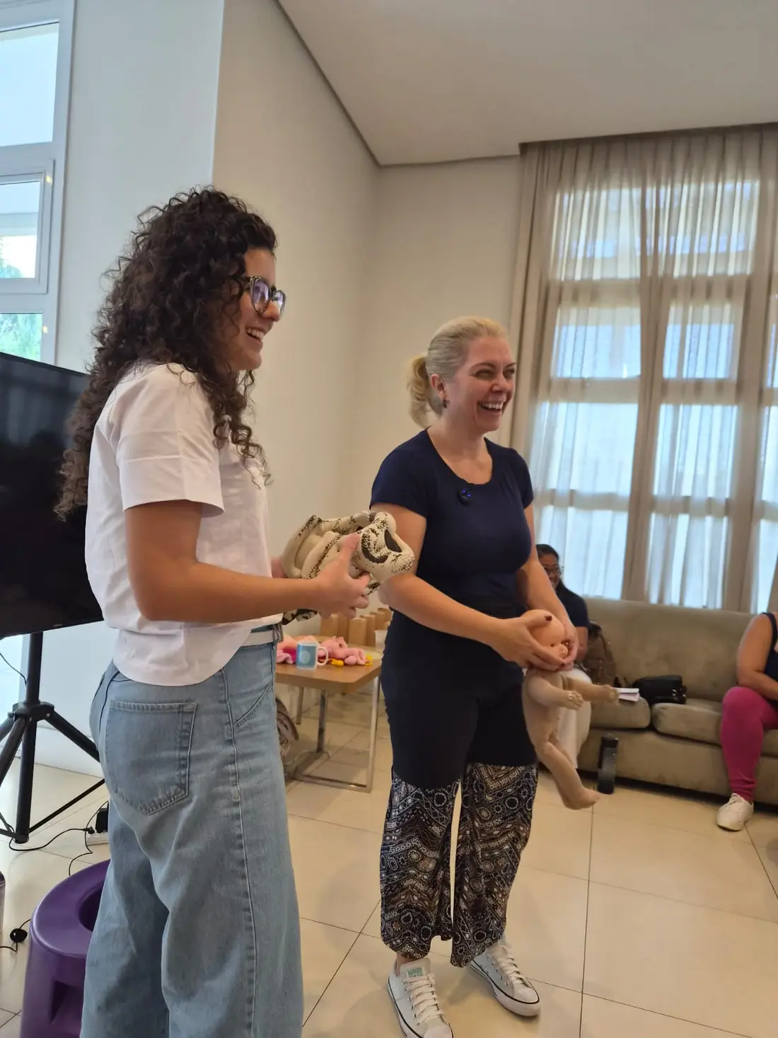 A docente segura um boneco de bebê e um modelo de placenta enquanto conversa com uma participante.